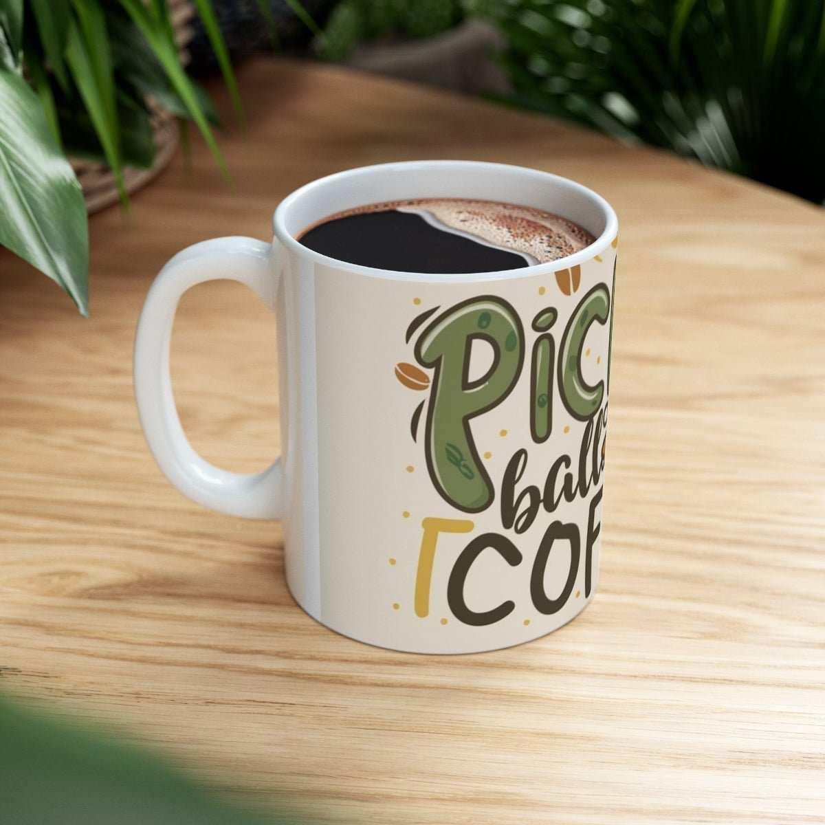 Ceramic mug with pickleball and coffee design on wooden table, greenery in background