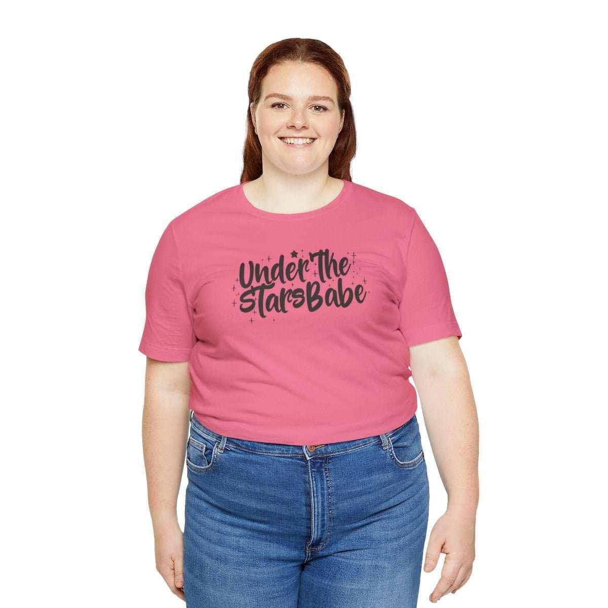 Woman wearing pink t-shirt with 'Under The Stars Babe' celestial text, casual fashion style.