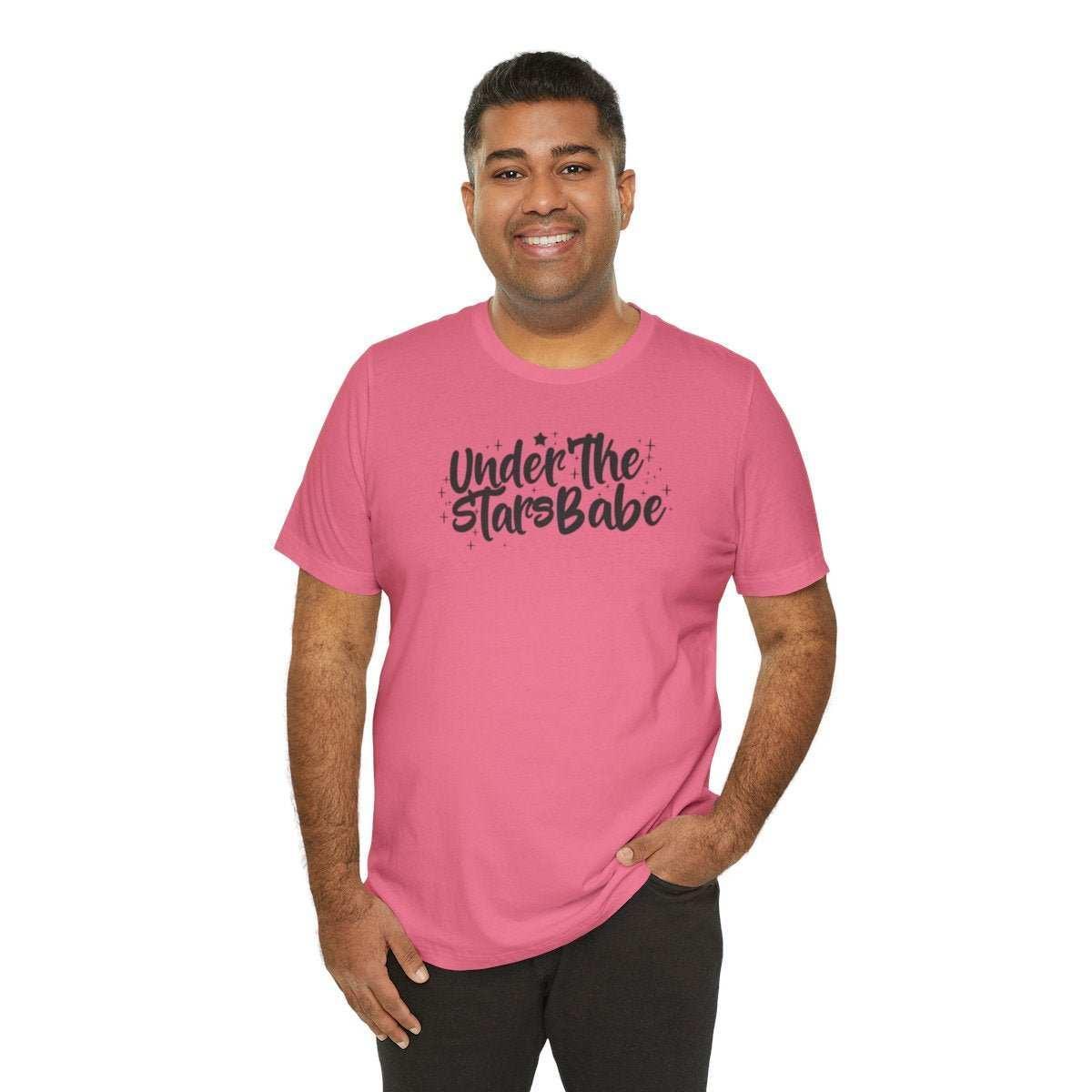 Smiling man wearing pink t-shirt with 'Under The Stars Babe' text and celestial accents